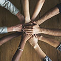 People standing in a circle, reaching into the middle and placing their hands on top of one another.