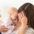 Women with her head in her hand holding a crying baby.