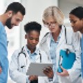 Diverse group of doctors and nurses looking together at a tablet in a doctor's hand.